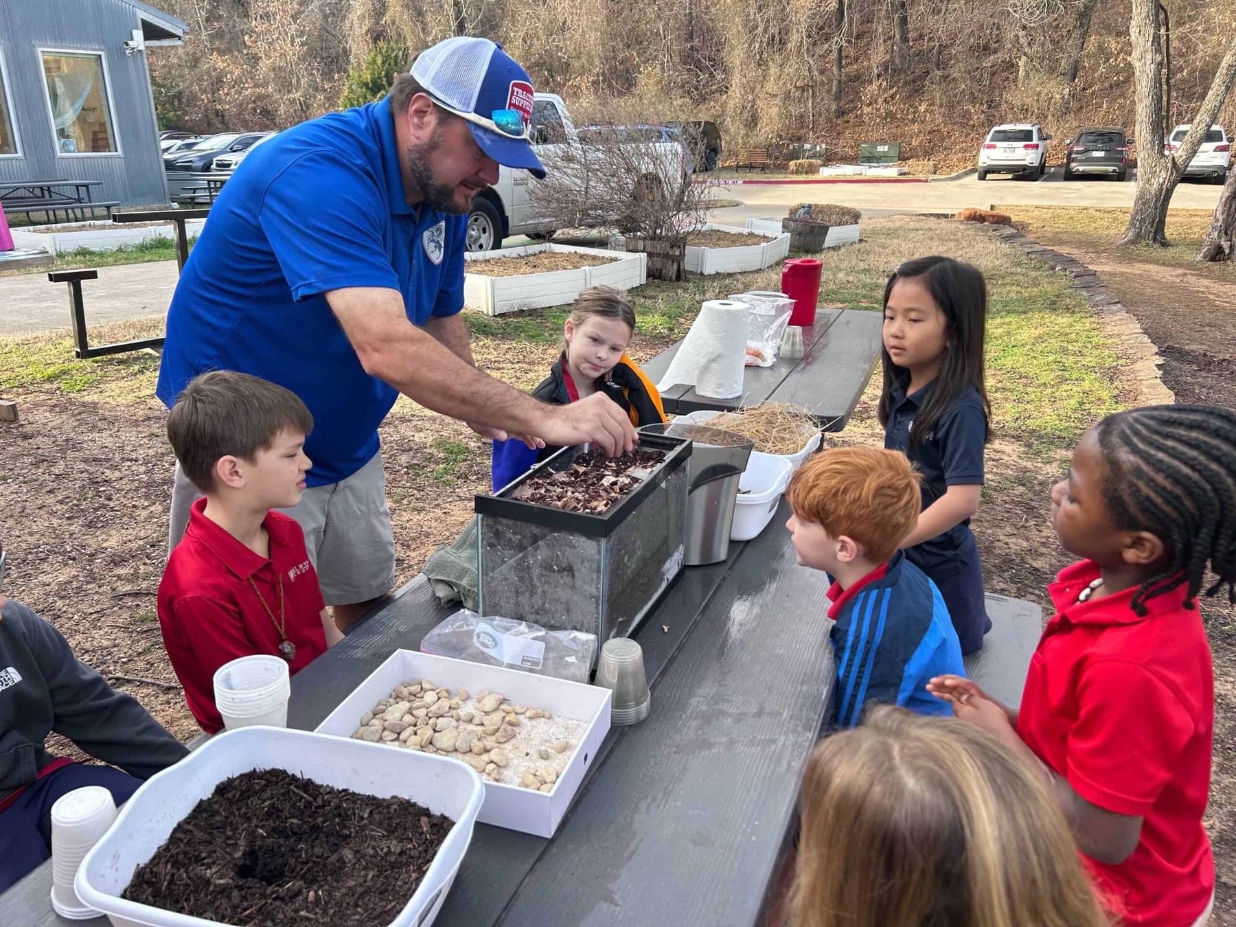 A Selwyn teacher works with a small group of students at an outdoor table on campus